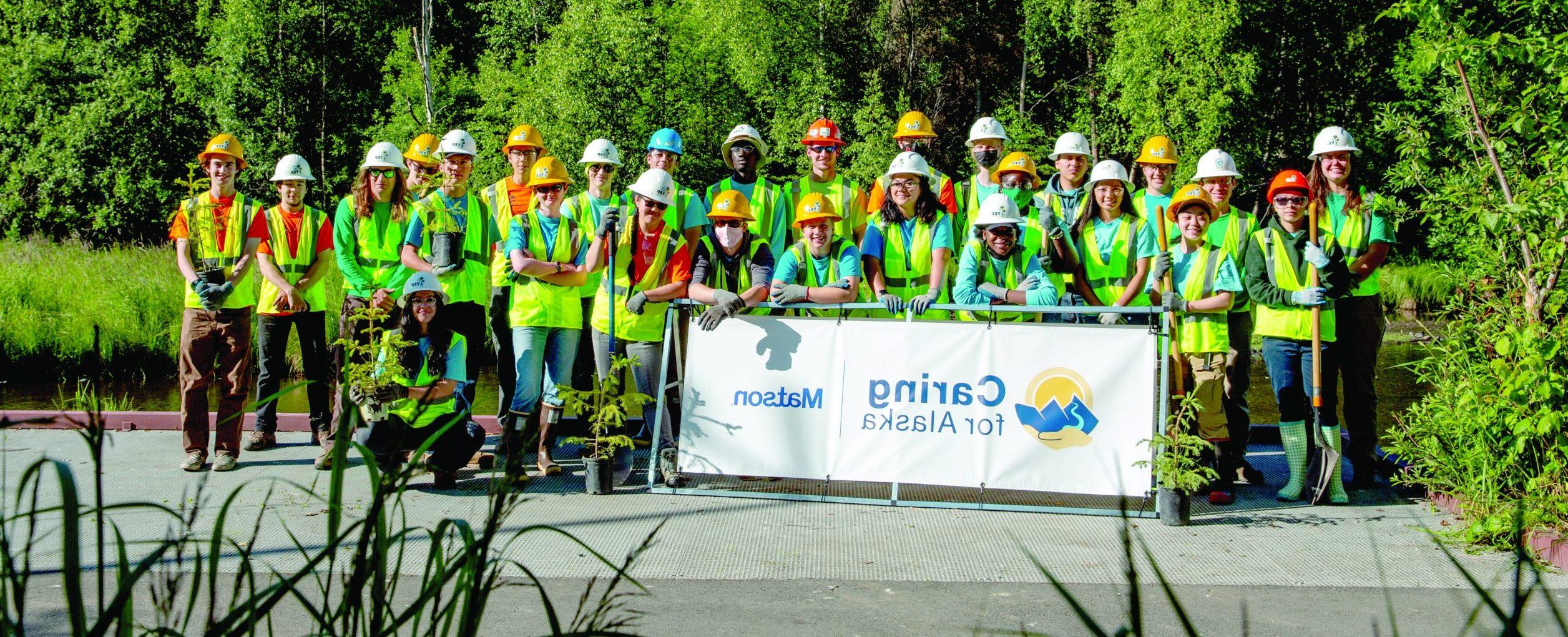 Youth Employment in Parks program participants wearing heardhats an dyellow vests pose with a Caring for Alaska sign.